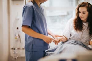 Nurse adjusting IV line for a woman resting in a hospital bed after mommy makeover surgery