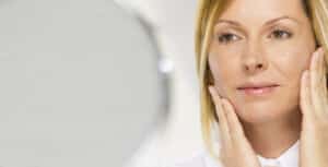 Woman touching the skin around her eyes, highlighting concerns that may be treated with upper or lower blepharoplasty.